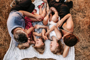 a family of four laugh on a picnic blanket in the grass