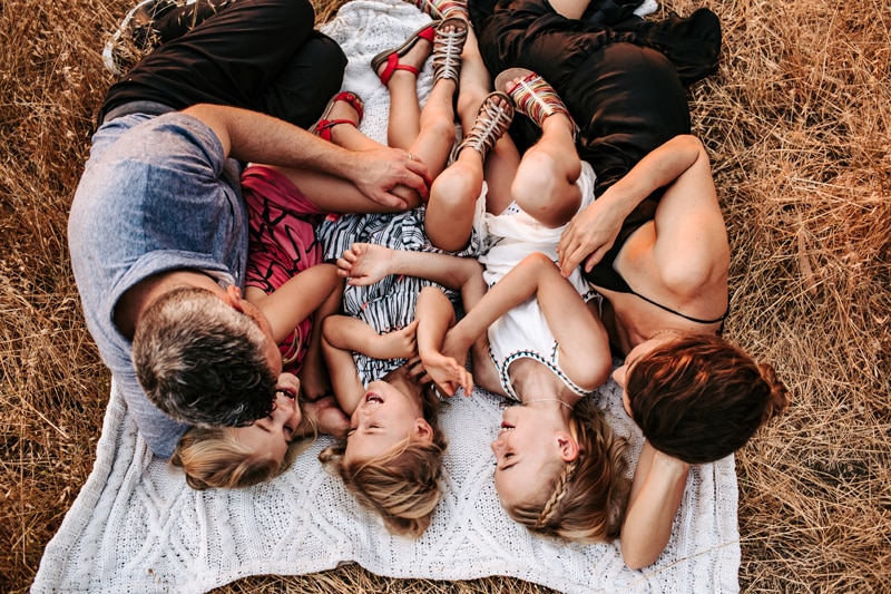 Family Photographer, mom, dad, and three daughters lay on a blanket in the grass