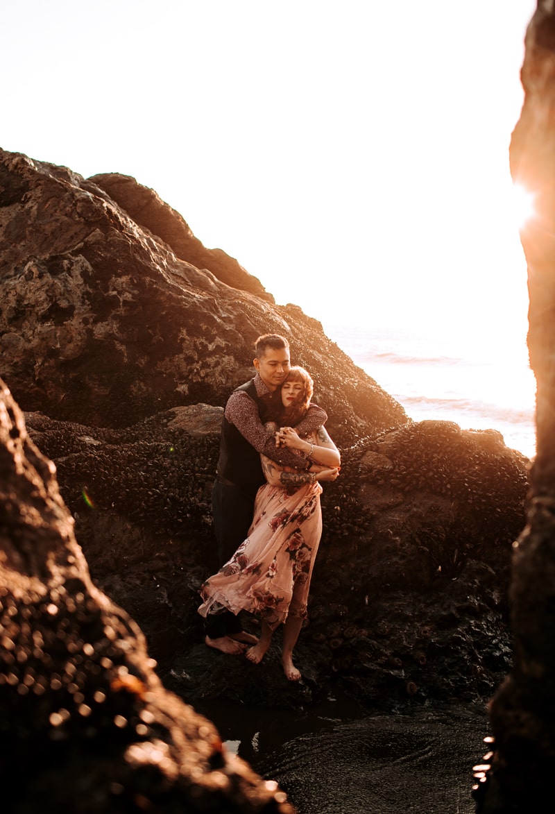 Couples Photographer, man and woman embrace on rocks near the ocean