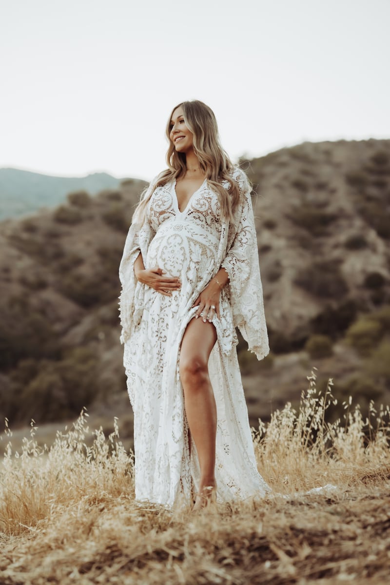Maternity Photographer, expecting woman stands on dry grassy hillside