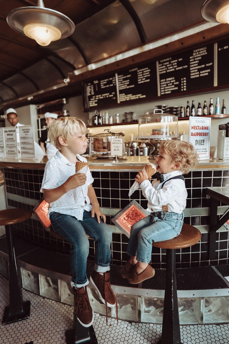 Family Photographer, two brothers sit on bar stools eating ice cream at an ice cream parlour