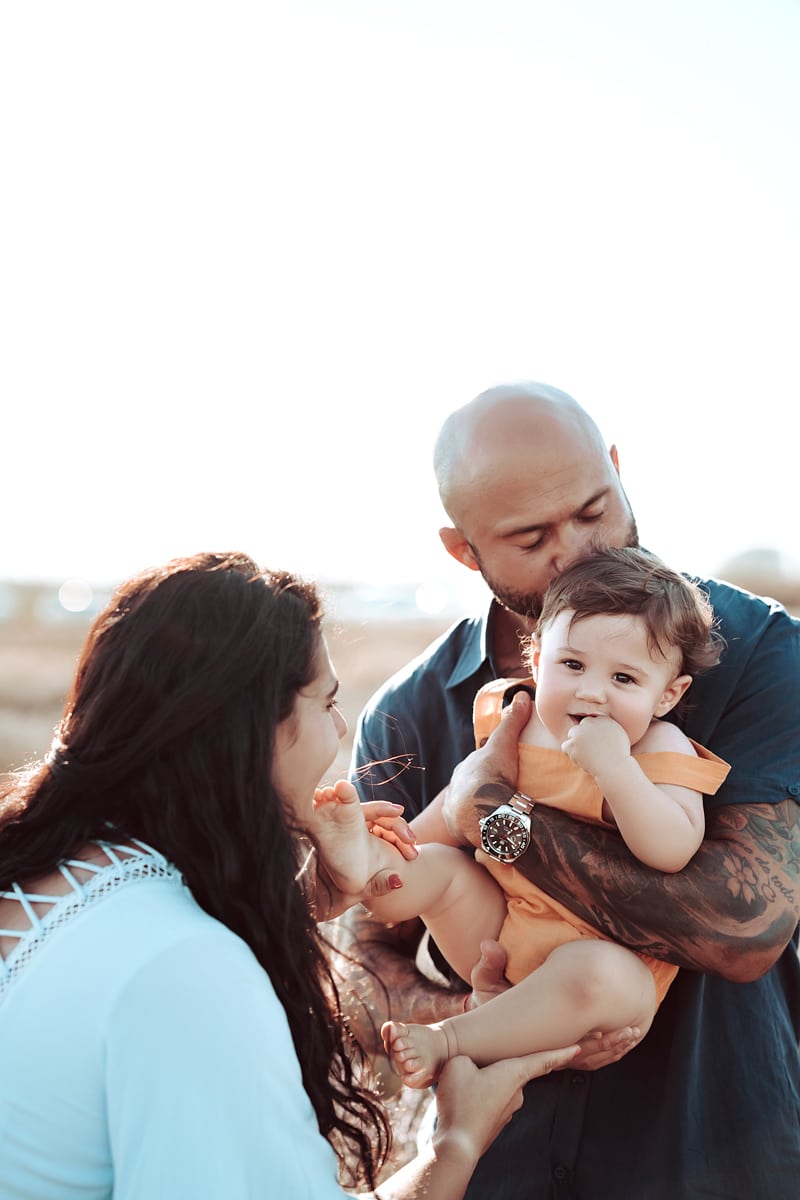 Family Photographer, dad kisses baby girl as he holds her, mom looks on happily