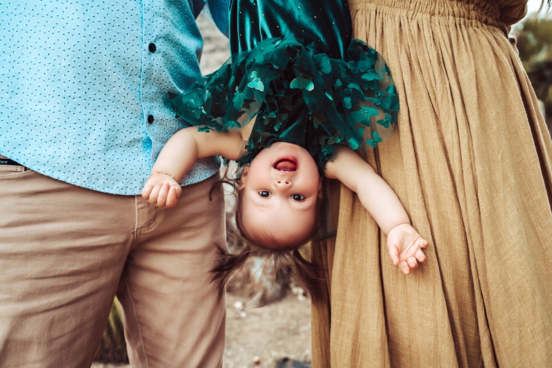 Family Photographer, a little girl is amused as she hangs upside down while being held by her parents