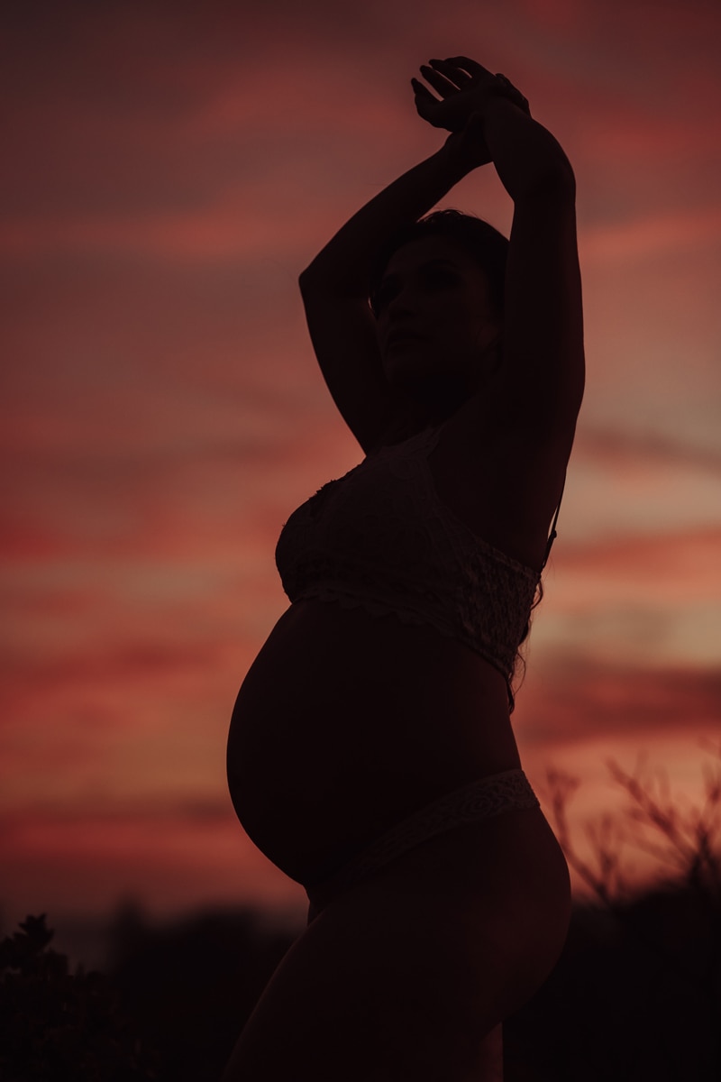 Maternity Photographer, the silhouette of an expecting mother stands agains a dusk sky