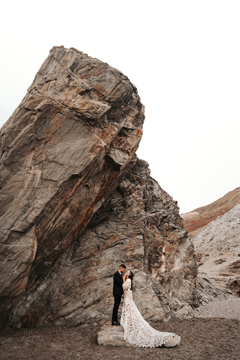 Wedding photographer, a man and woman look into each other's eyes, they stand before large rocks within the mountains