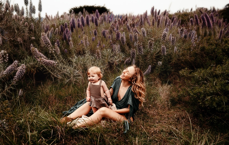 Family Photographer, a young mother holds baby as they sit among the wild lavender
