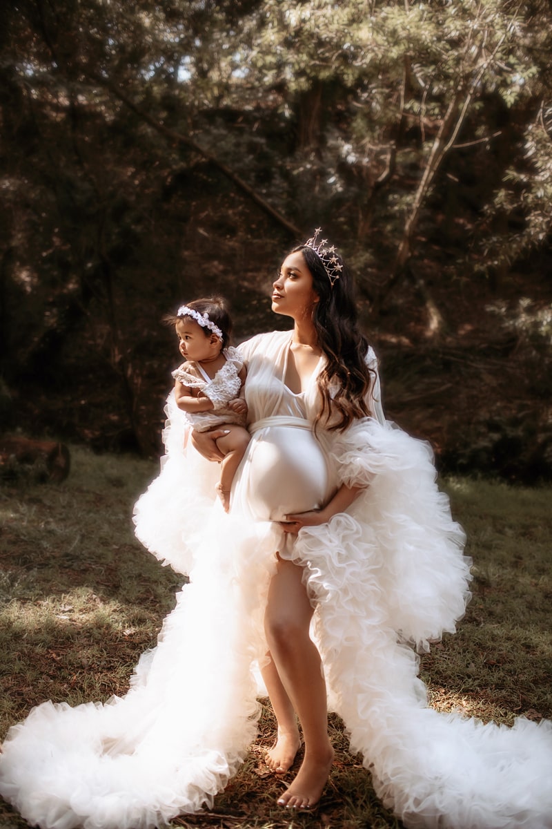 Maternity Photographer, a proud expecting mother holds child and wears a white dress with big white boa
