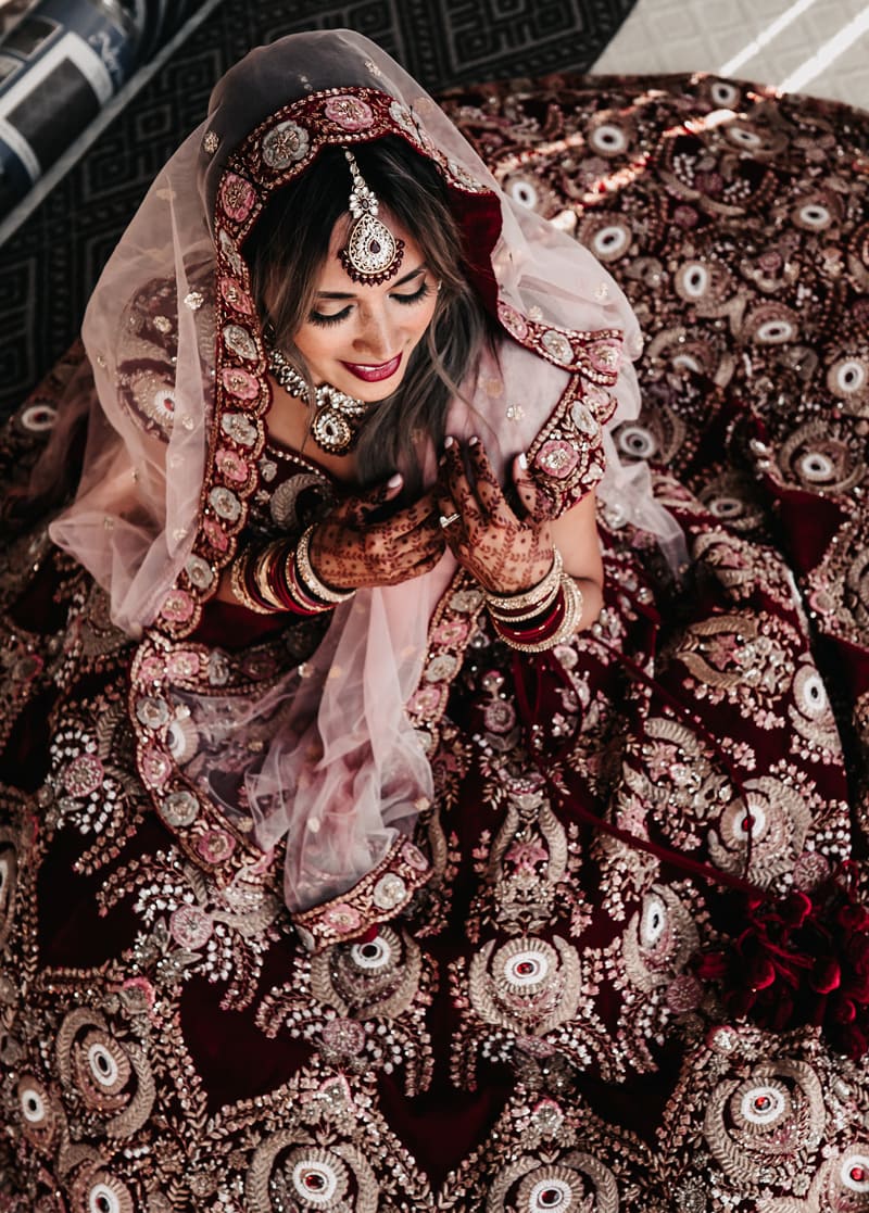Wedding Photographer, a bride sits smiling, she wears an ornate dress and has henna designs painted on her hands