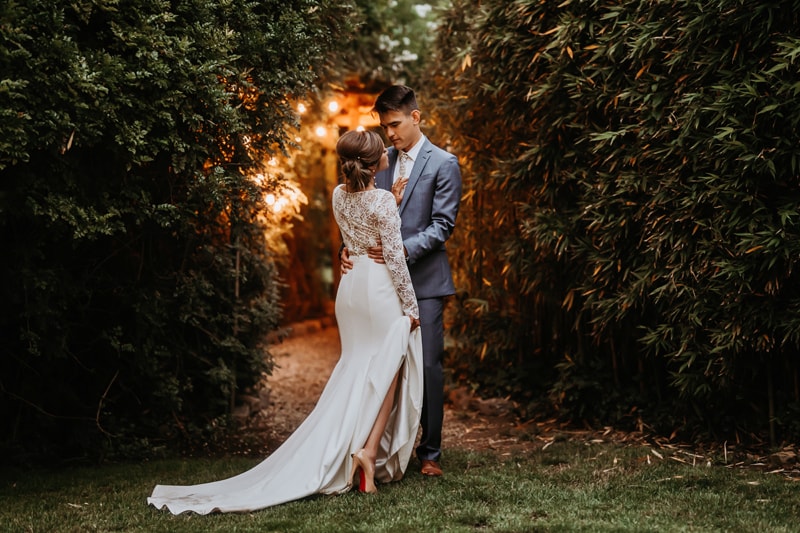 Wedding Photographer, a bride and groom hold each other in a garden pathway illuminated by string lights