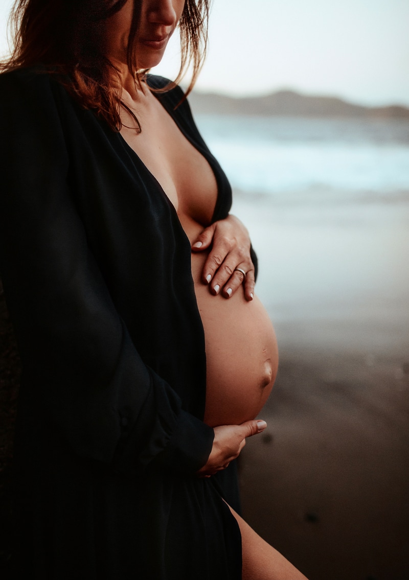 Maternity Photographer, a woman holds her pregnant belly near the ocean