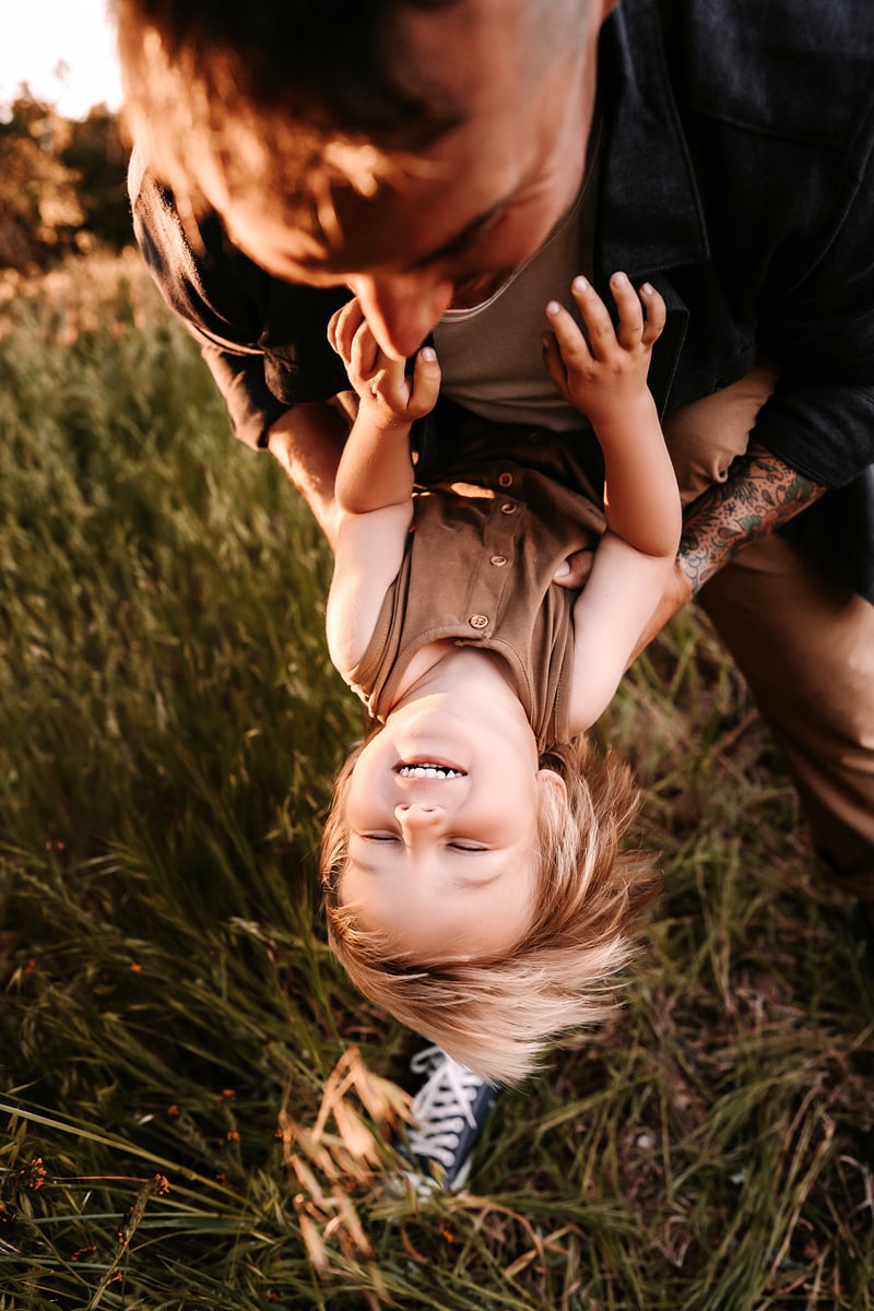 Family Photographer, a child looks amused as dad swings her over the grass
