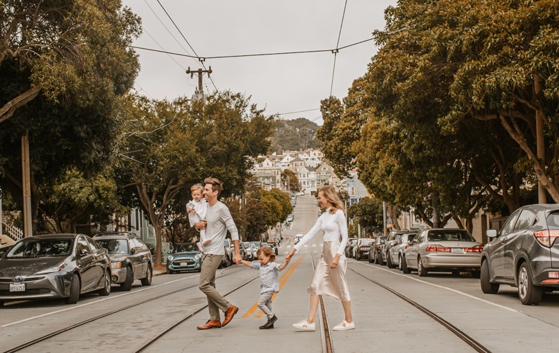 a family of four walks across a city street, the trolley's tracks beneath them