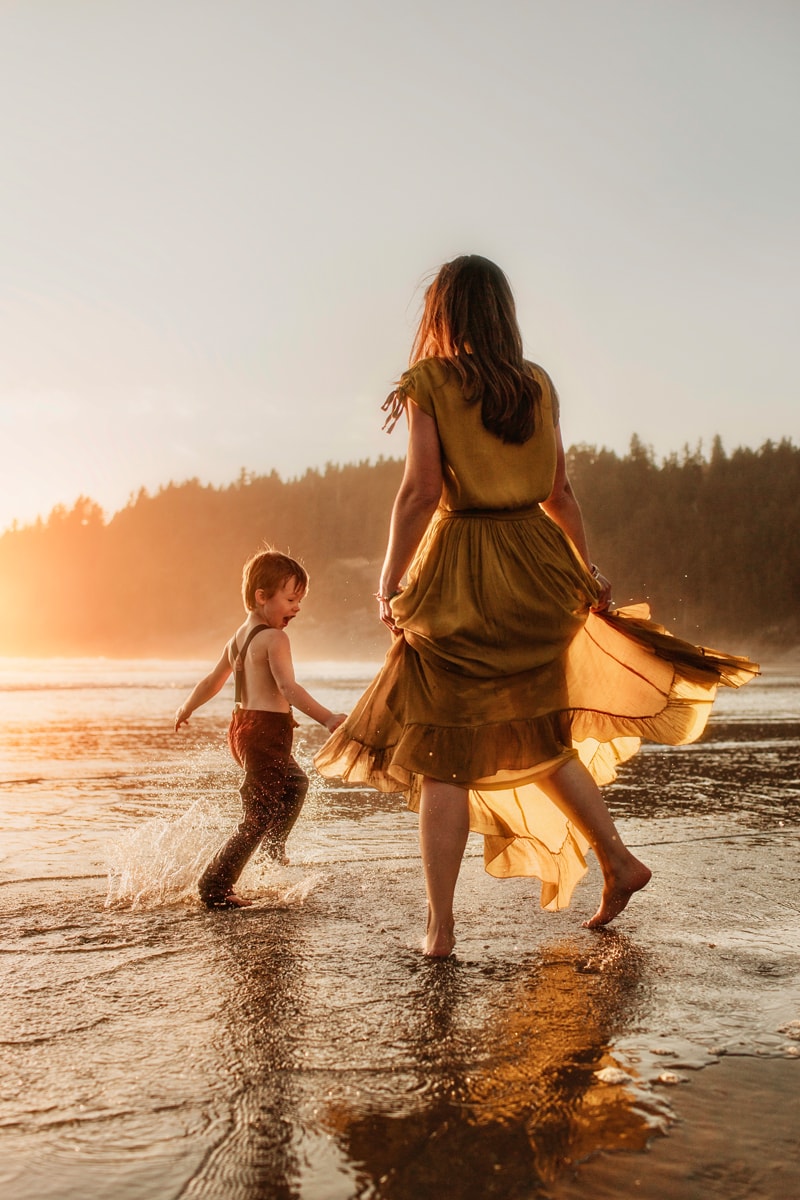 Family Photographer, a young mother chases her young sun through the ocean's tide at golden hour