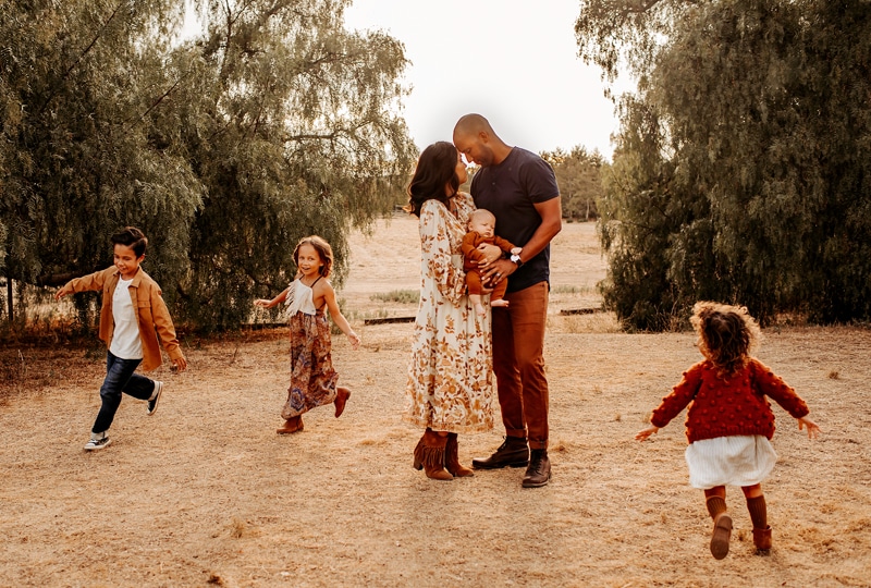 Family Photographer, Dad and mom hold their new baby, their other three children dance around them