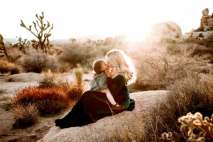 A woman kisses her child as she sits in the desert before a Joshua tree