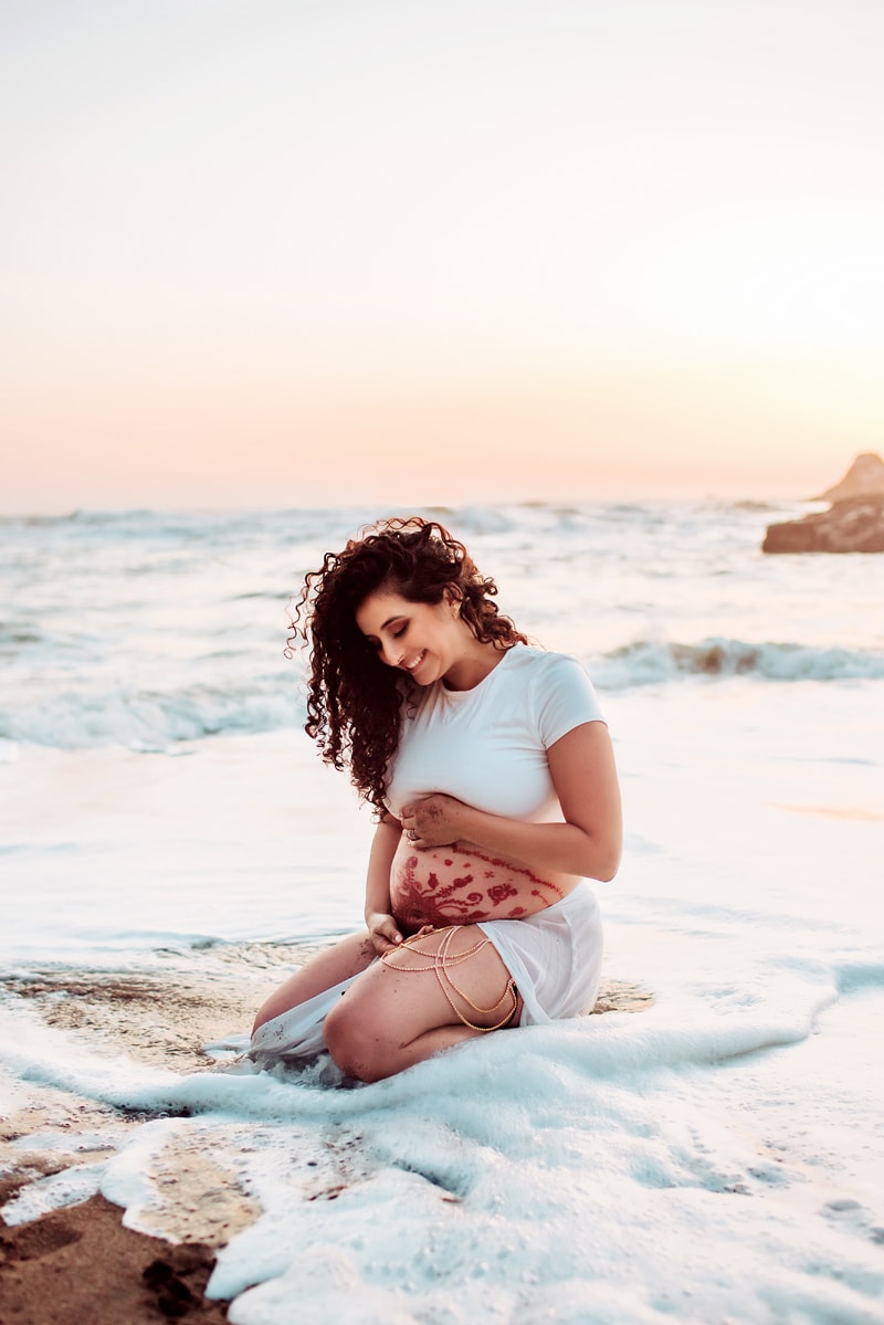 Maternity Photographer, an expecting mother kneels into the beaches quiet tides