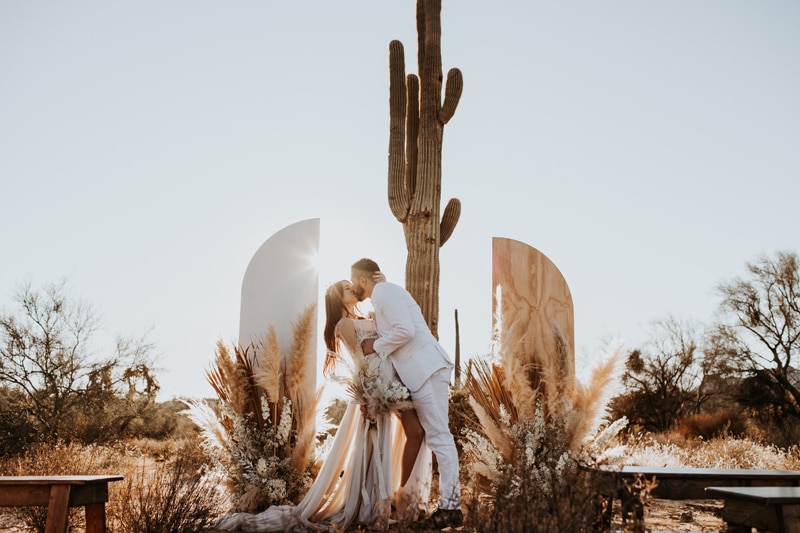 Elopement Photographer, bride and groom kiss before ornate arbor in the desert