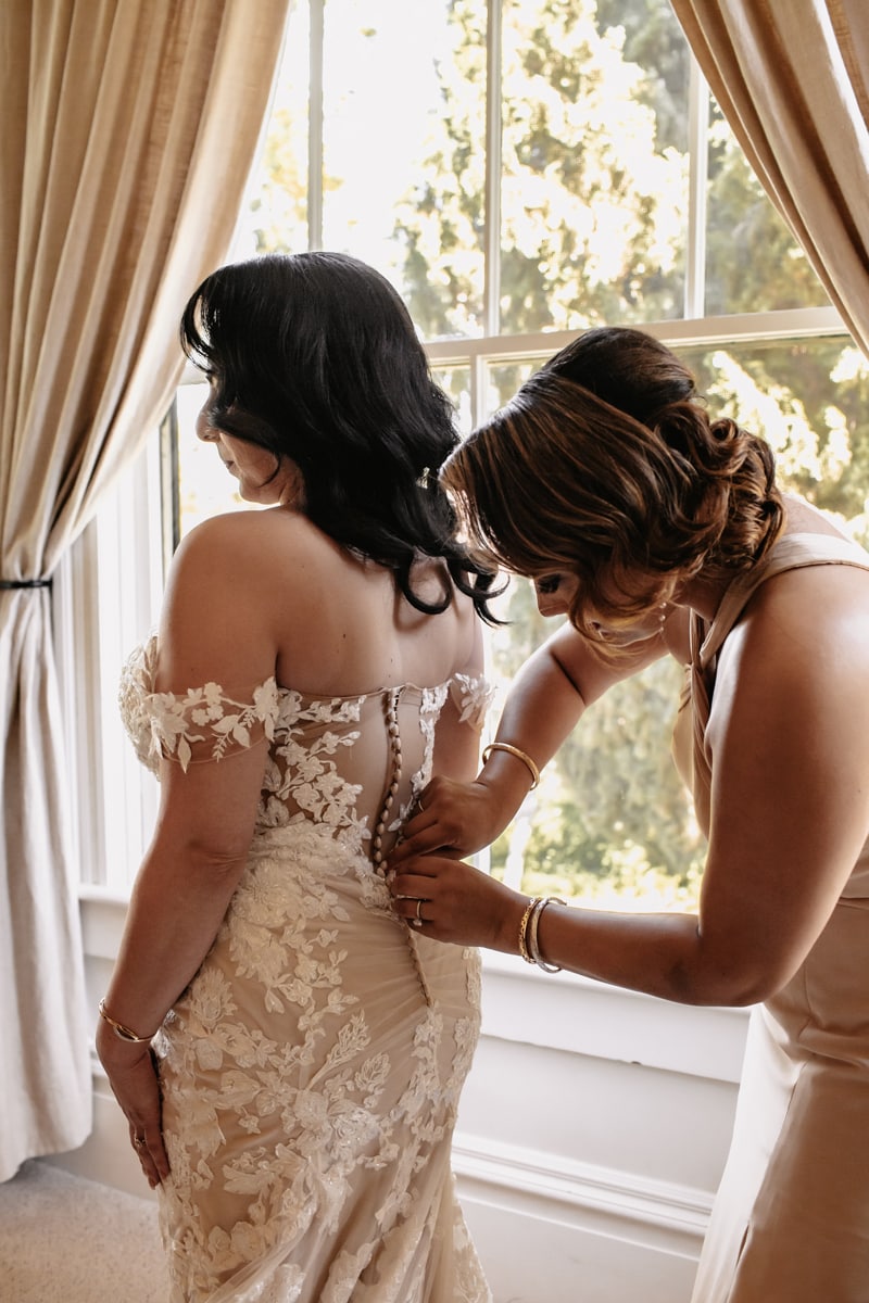 Wedding Photographer, a woman helps bride with her dress before the ceremony