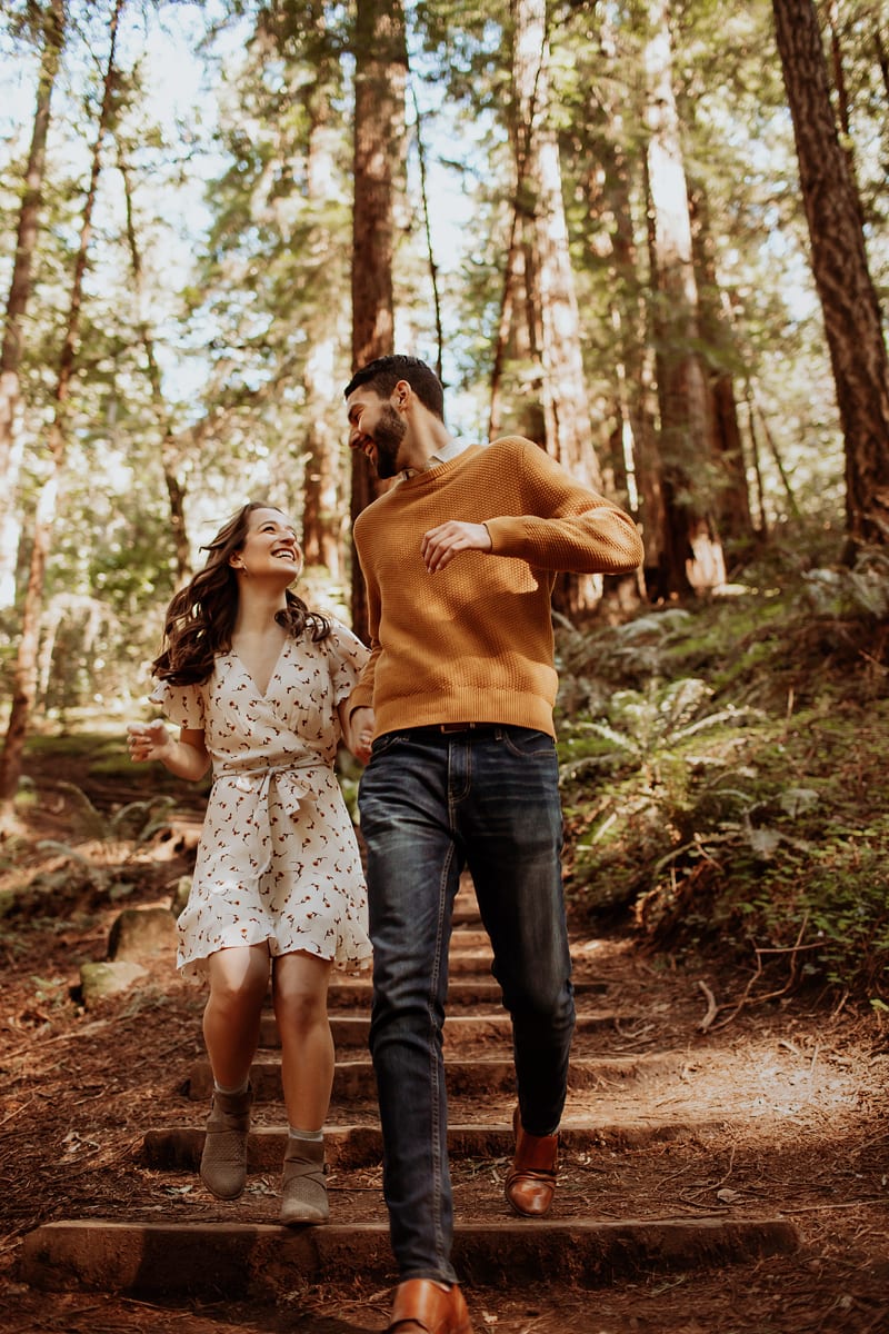 Couples Photographer, man and woman hold hands as they walk down trail in the forest