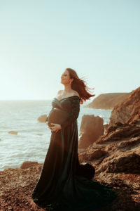 Maternity Photographer, an expecting woman stands on the rocks near the ocean