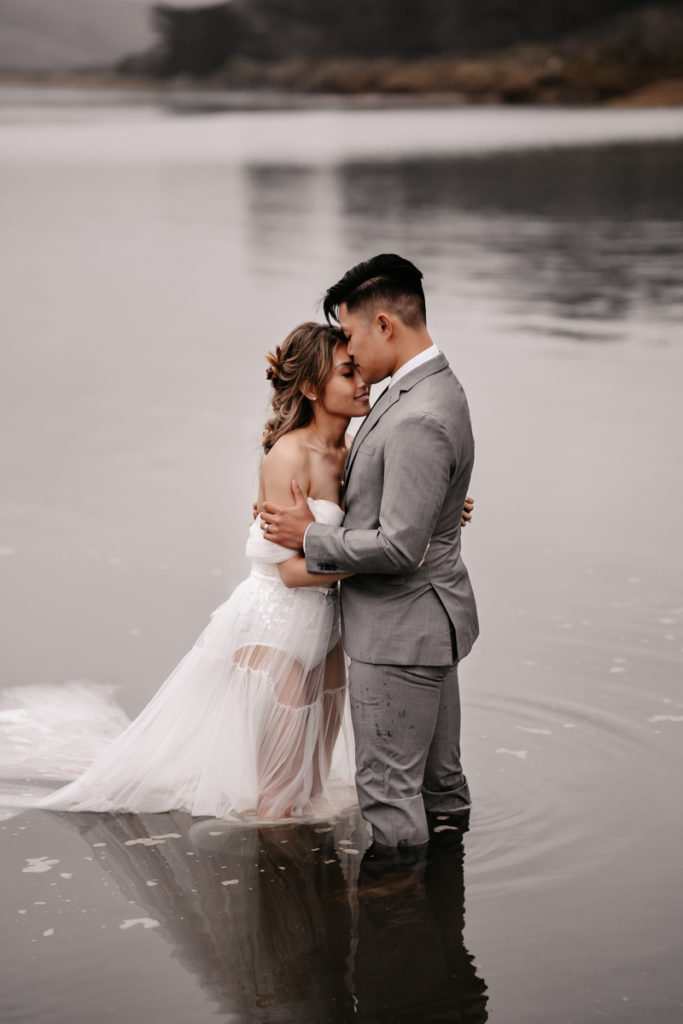 Wedding Photographer, a bride and groom stand holding each other knee deep in a quiet lake