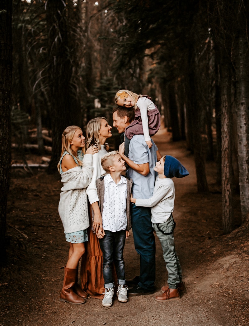 Family Photographer, a husband and lean into each other, their four kids around them, they are in the forest