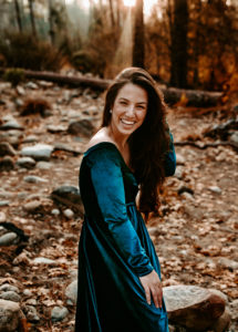 a woman in a dress smiles as if laughing in a forest environment