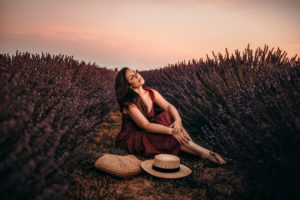 a woman sits comfortably on the ground near wild lavender at dusk