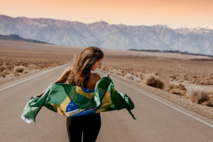 a woman walks down a road in the desert, she holds a flag behind her